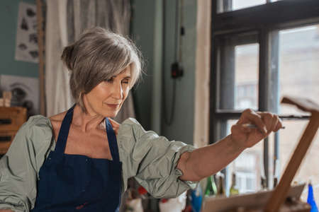 Woman wearing apron measuring with pencil during the drawing while standingの写真素材