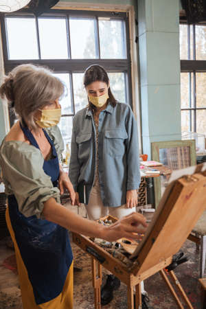 Mature female artist standing in front of the easel with her student and teaching herの写真素材