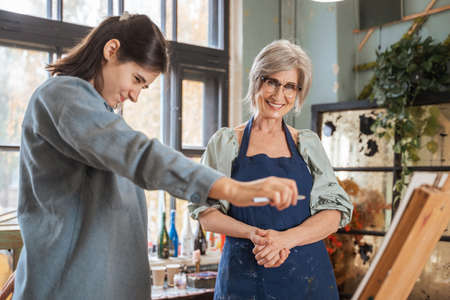 Girl holding pencil and measuring while standing in front of easel and drawing somethingの写真素材