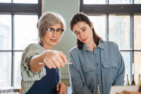 Female tutor holding pencil while standing in front of the easel with her student girlの写真素材