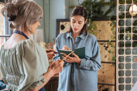 Woman writing something at the notebook while standing at the lesson at the art studioの写真素材