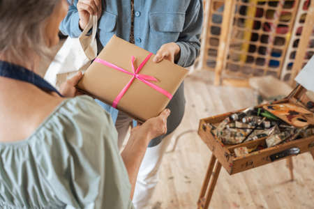 Woman standing in front her student girl and taking present with pink ribbonの写真素材