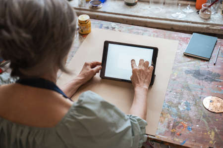Woman typing at the tablet screen while sitting at the table