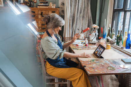 Elderly female tutor waving to her students while giving online lesson at the tablet