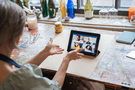 Teacher gesturing while chatting with her students via video call at the tabletの写真素材