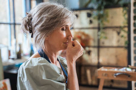 Elderly woman keeping her eyes closed and doing breathing exercise while closes nostrilの写真素材