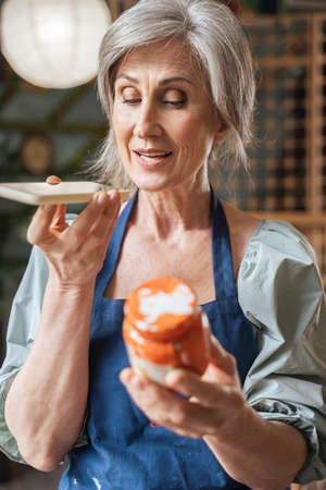 Senior woman holding bottle with acrylic paint and recording voice message to somebodyの写真素材
