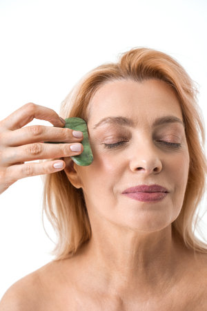 Elderly woman doing self massage with rose quartz gua sha stone while closed her eyesの写真素材