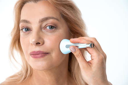 Mature woman with clean face skin holding massager in her handの写真素材