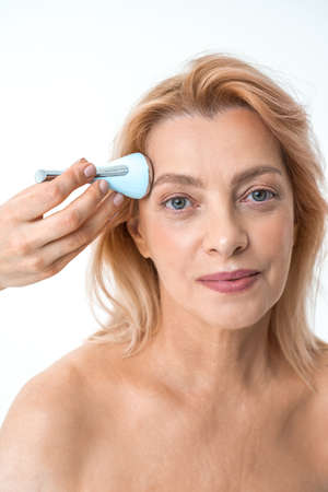 Mature woman with perfect skin using device for taking care of her faceの写真素材