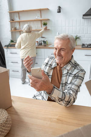 Retirement man holding smartphone and gesturing while chatting with somebody