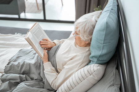 Cute retirement woman is reading in bedroomの写真素材