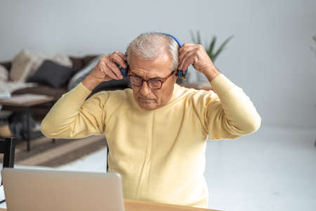 Concentrated senior man taking on headset before video call using laptop at homeの写真素材