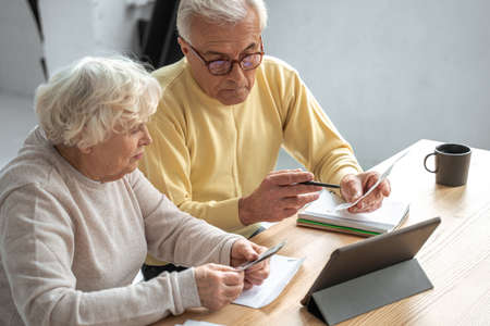 Mature couple sitting and managing expenses at homeの写真素材