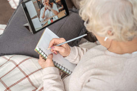 Elderly woman using electronic tablet at home while studying with couch