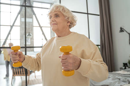 Energetic sporty mature woman exercising at home, while doing bicep curlsの写真素材
