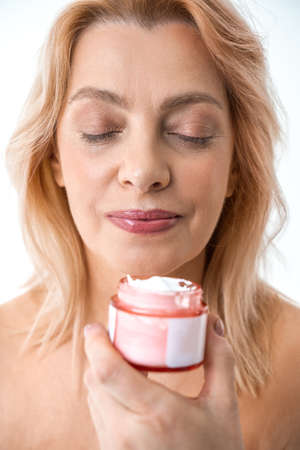 Smiling woman applying moisturizing cream on her faceの写真素材