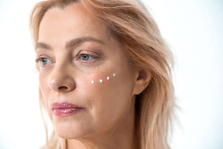 Attractive serious woman applying moisturizer cream on her faceの写真素材