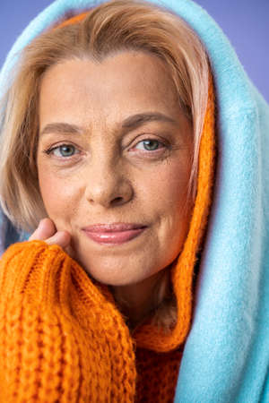 Mature woman with nude makeup smiling positively isolated on violet backgroundの写真素材