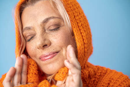 Retired female wearing warm knitted clothes posing with closed eyes and charming smileの写真素材