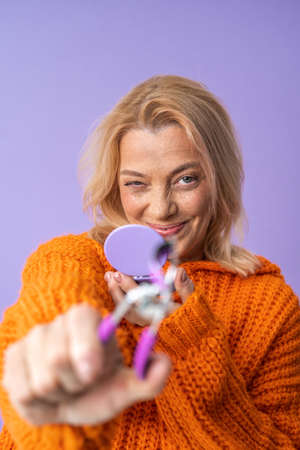 Elderly woman stretching to the camera eyelash curler while holding mirrorの写真素材