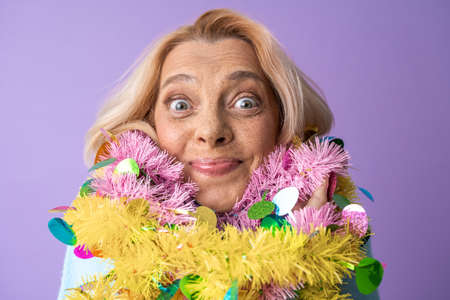 Overjoyed mature woman wrapped at the bright garland looking at the cameraの写真素材