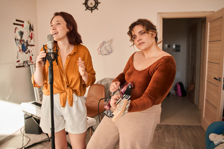 Female musician feeling involved while playing guitar at home at her roomの写真素材