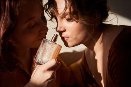 Two girls sniffing perfumes while sitting near each other at home at the weekendの写真素材