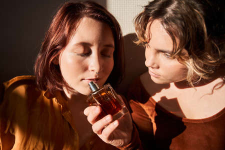 Do you like. Portrait view of the cute  woman giving perfumes to her lovely girlfriend. She sniffing it with closed eyes. Stock photoの写真素材