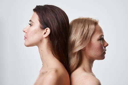 Brunette and blonde women standing back-to-back and posing to the cameraの写真素材