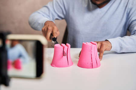 Blogger guy holding knife and preparing destroying pink molds from kinetic sand