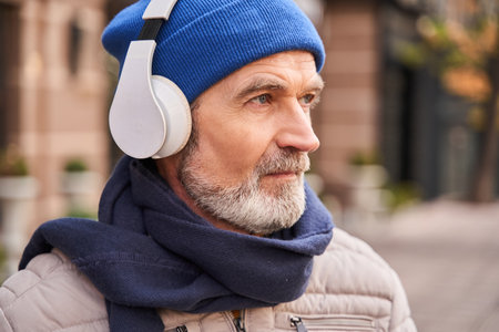 Calm senior bearded man looking away while listening musicの写真素材