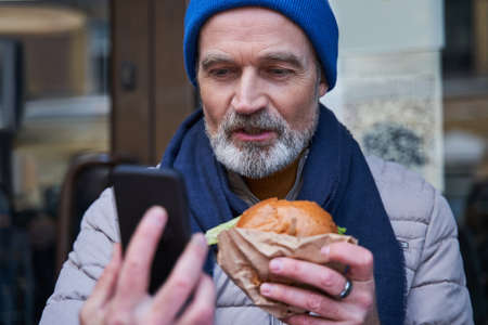 Mature man having call with somebody at the smartphone while sitting at the tableの写真素材