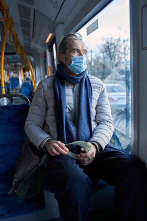 Senior passenger wearing protective mask looking at the window at public transportの写真素材