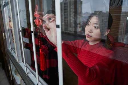 Asian woman putting traditional pendant while decorating flat to the Chinese New Year