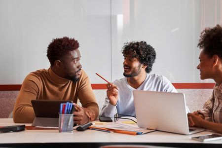 Young students or coworkers laughing while using digital devices and discussing their workの写真素材