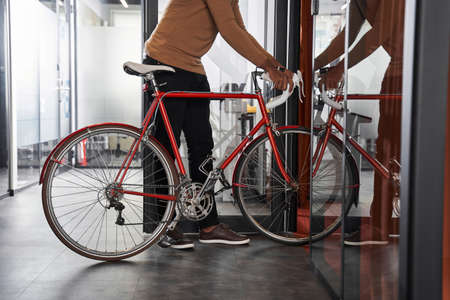 Multiracial businessman entering inside the coworking room with his bikeの写真素材