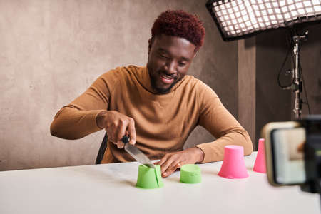 Guy smiling toothy and holding knife while cutting kinetic sand during recording video