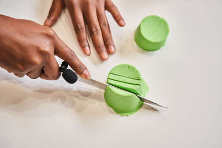 Multiracial guy chopping molds from green kinetic sand and enjoying of the sound
