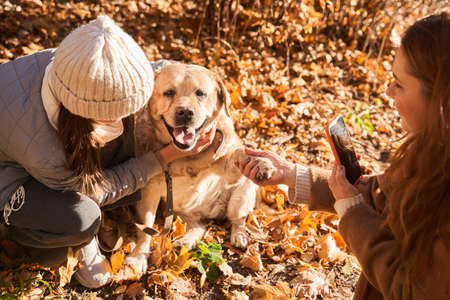 Woman shooting at the smartphone her daughter with her fluffy dogの写真素材