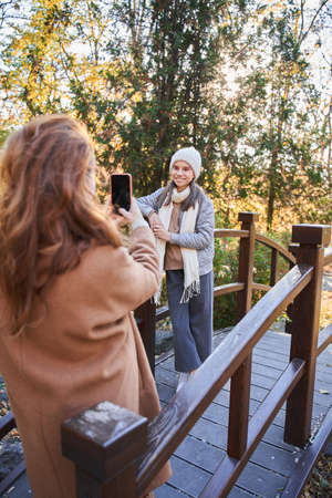 Woman making photo session for her daughter while standing at the autumn parkの写真素材