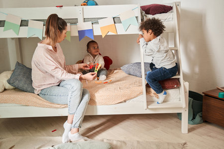 Single caucasian mother playing with her two funny son while sitting at the bed at homeの写真素材