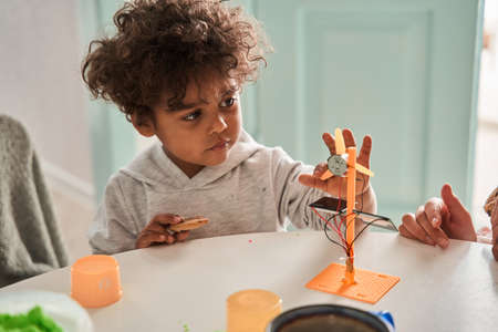 Multiracial boy playing at the table at the kitchen while looking attentively at the toy