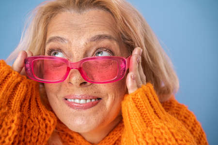 Vivacious freckled woman wearing modern pink sunglasses looking up