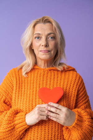 Romantic woman wearing orange pullover holding heart symbol at her handsの写真素材