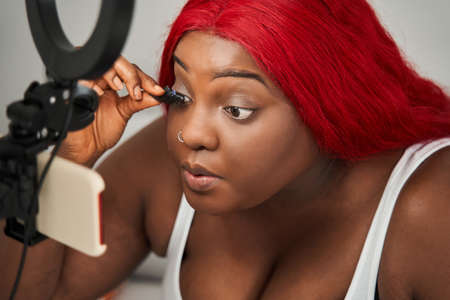 Woman with red hair applying eyelashes at her face while recording beauty blogの写真素材