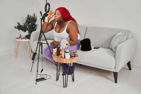 Female blogger with red hair looking at the camera of smartphone and preparing make upの写真素材