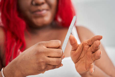 Oversize red haired woman doing manicure with nail file while spending time at hom