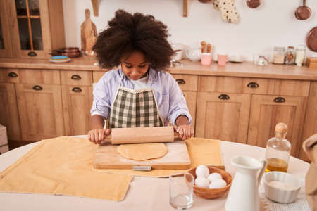Female multiracial child kneading dough on lightly table during the weekend