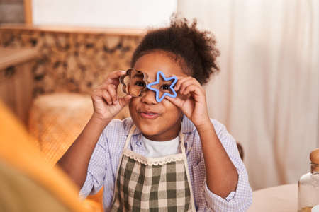 Multiracial child looking from the baking forms and feeling happy while cooking with her motherの写真素材